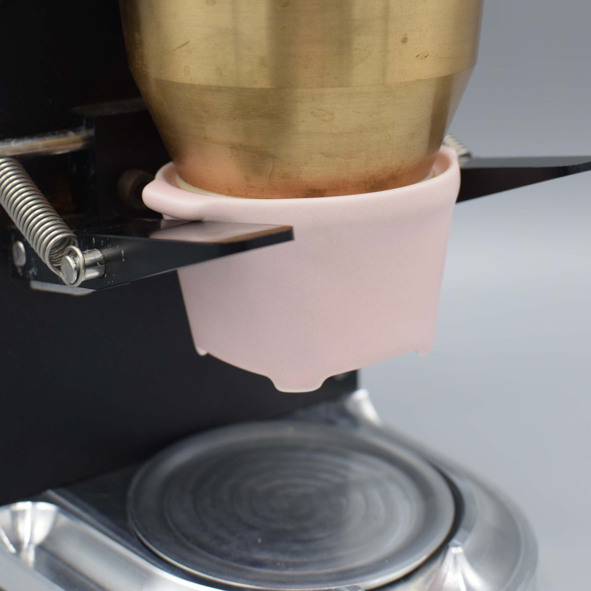 Close-up of a brass object being held by a pink clamp on a metallic surface.