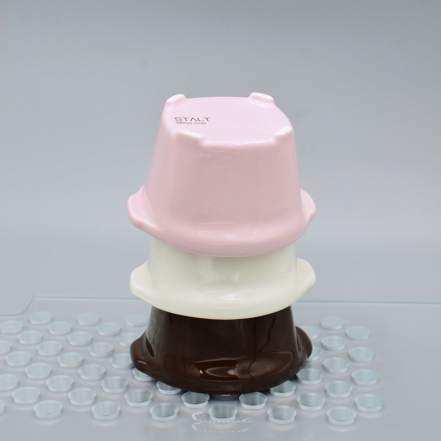 Stack of pink, white, and brown plastic containers on a gray surface with small clear cups.