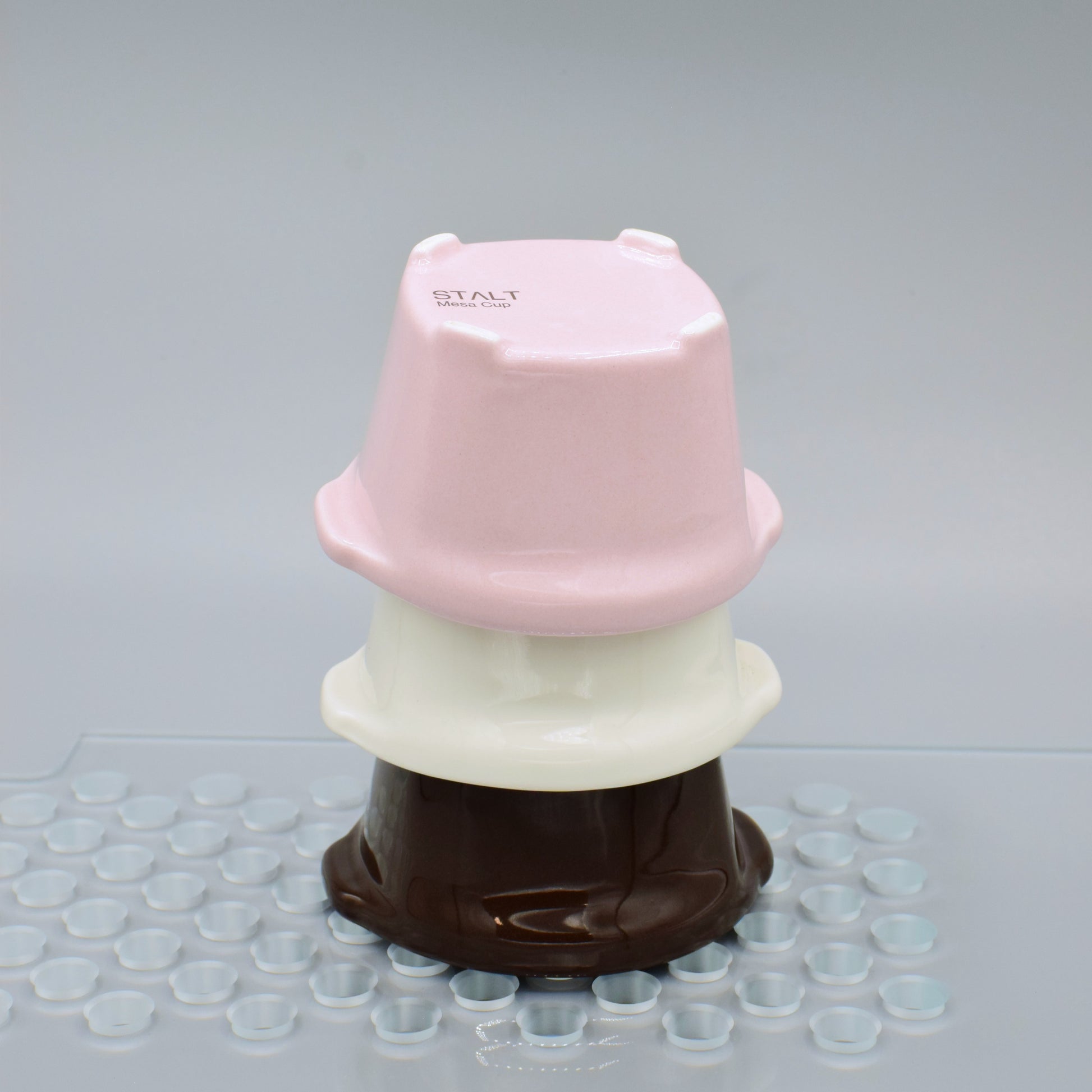 Stack of pink, white, and brown plastic containers on a gray surface with small clear cups.
